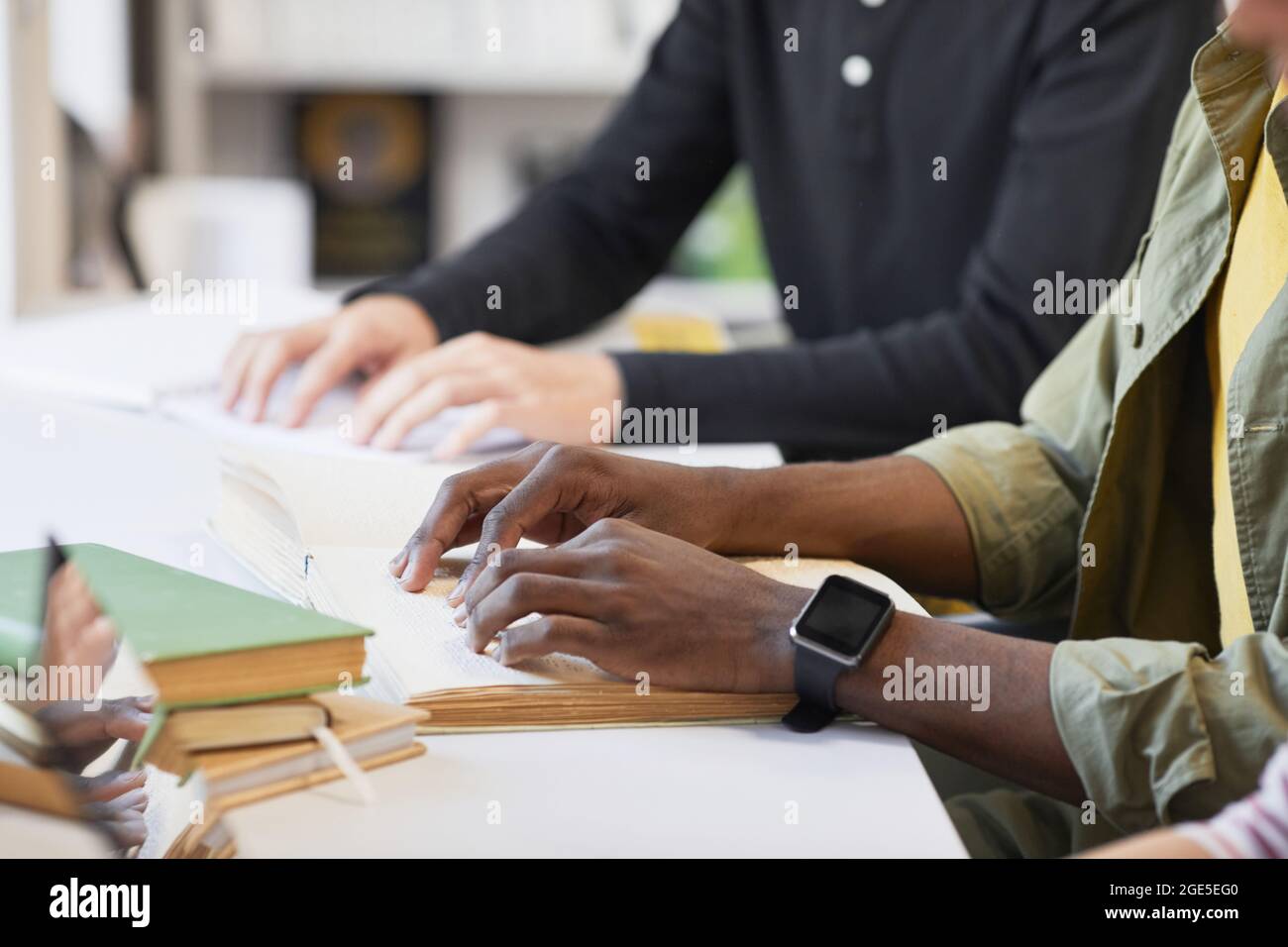 Side view closeup of inclusive group of students with young man reading braille book in library Stock Photo