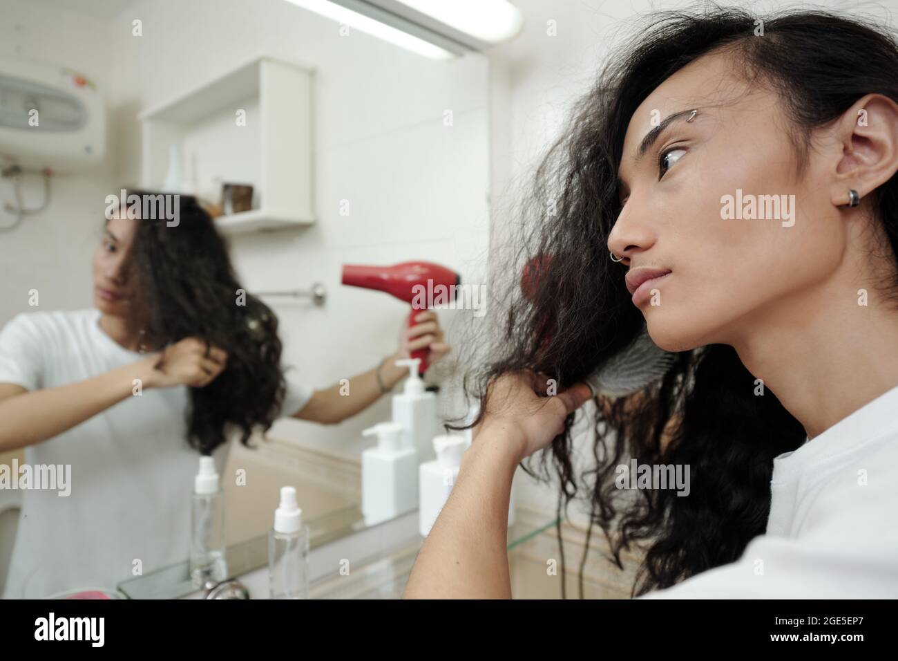 Handsome young man blowing out his long curly hair in front of bathroom