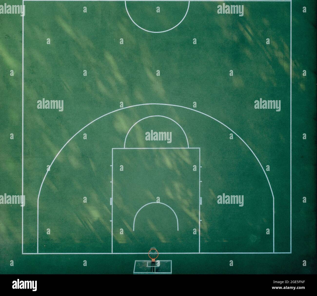 Green basketball playground with white markings and morning shadows