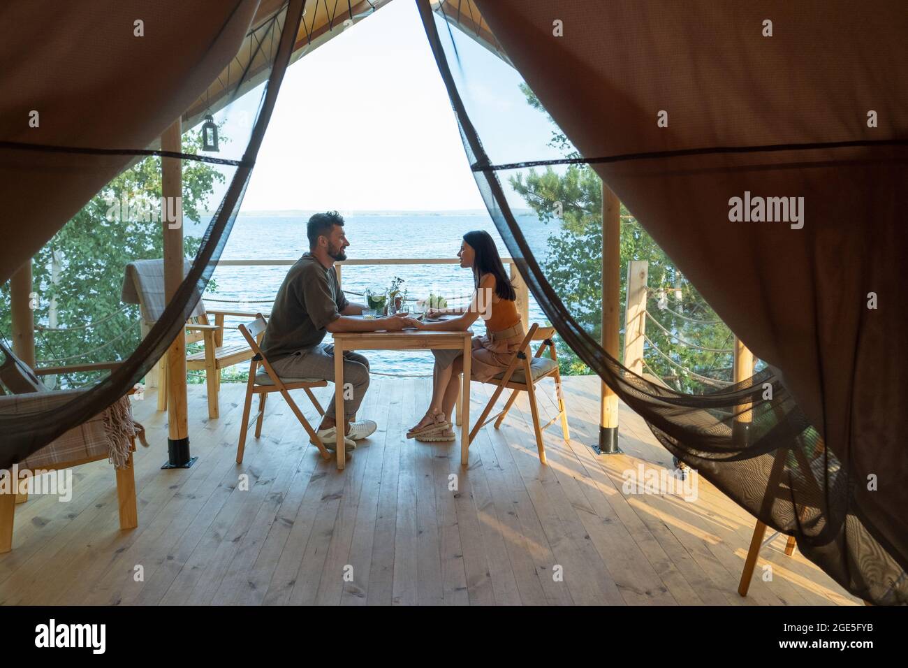 Young romantic couple holding by hands while enjoying breakfast on terrace by seaside Stock Photo