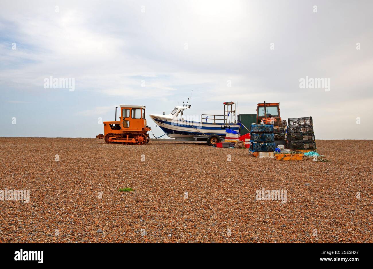 Inshore fishing boats with tractors, trailers, and equipment, beached above high water mark at Cley-next-the-Sea, Norfolk, England, United Kingdom. Stock Photo