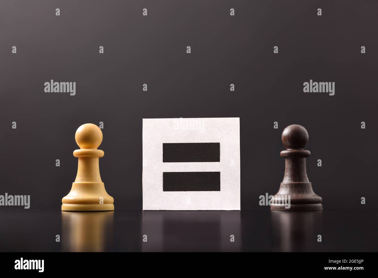 Concept of equality between people with black and white chess pieces with dark background and placard with equal sign Stock Photo