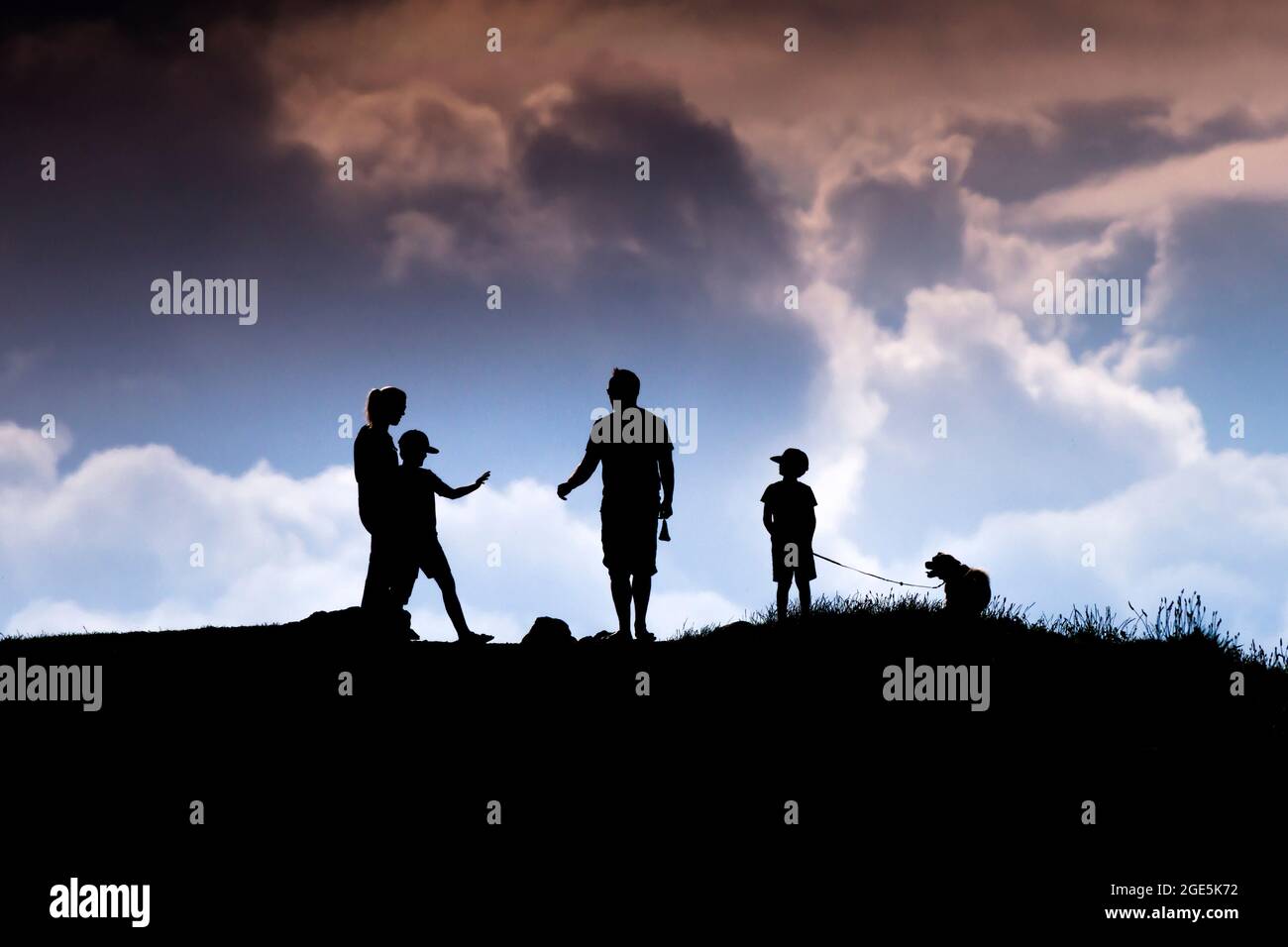 A family and their pet dog seen in silhouette walking in the late evening sunlight on Pentire Point East in Newquay in Cornwall. Stock Photo