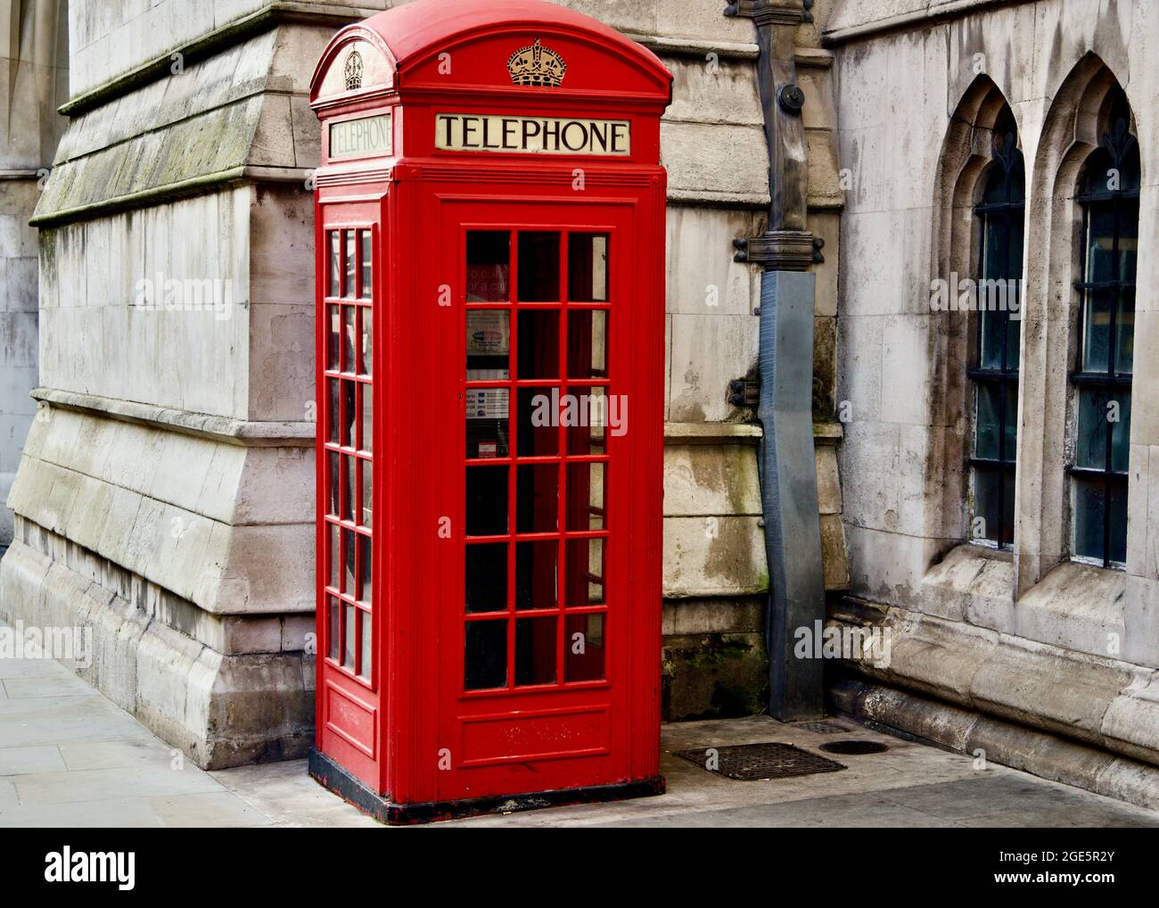 Phone Box - London Iconic phone box in bright red standing against a classical style building with arched windows and traditional stonework. Stock Photo