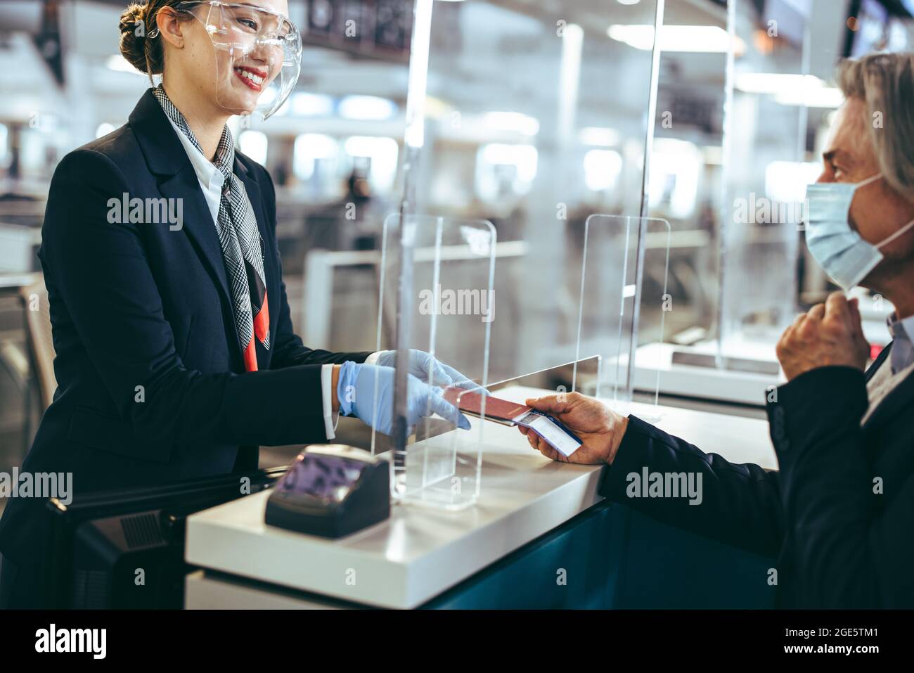 Man holding boarding pass and passport at airline check-in desk at international airport during pandemic. Airport employee in face shield and passenge Stock Photo