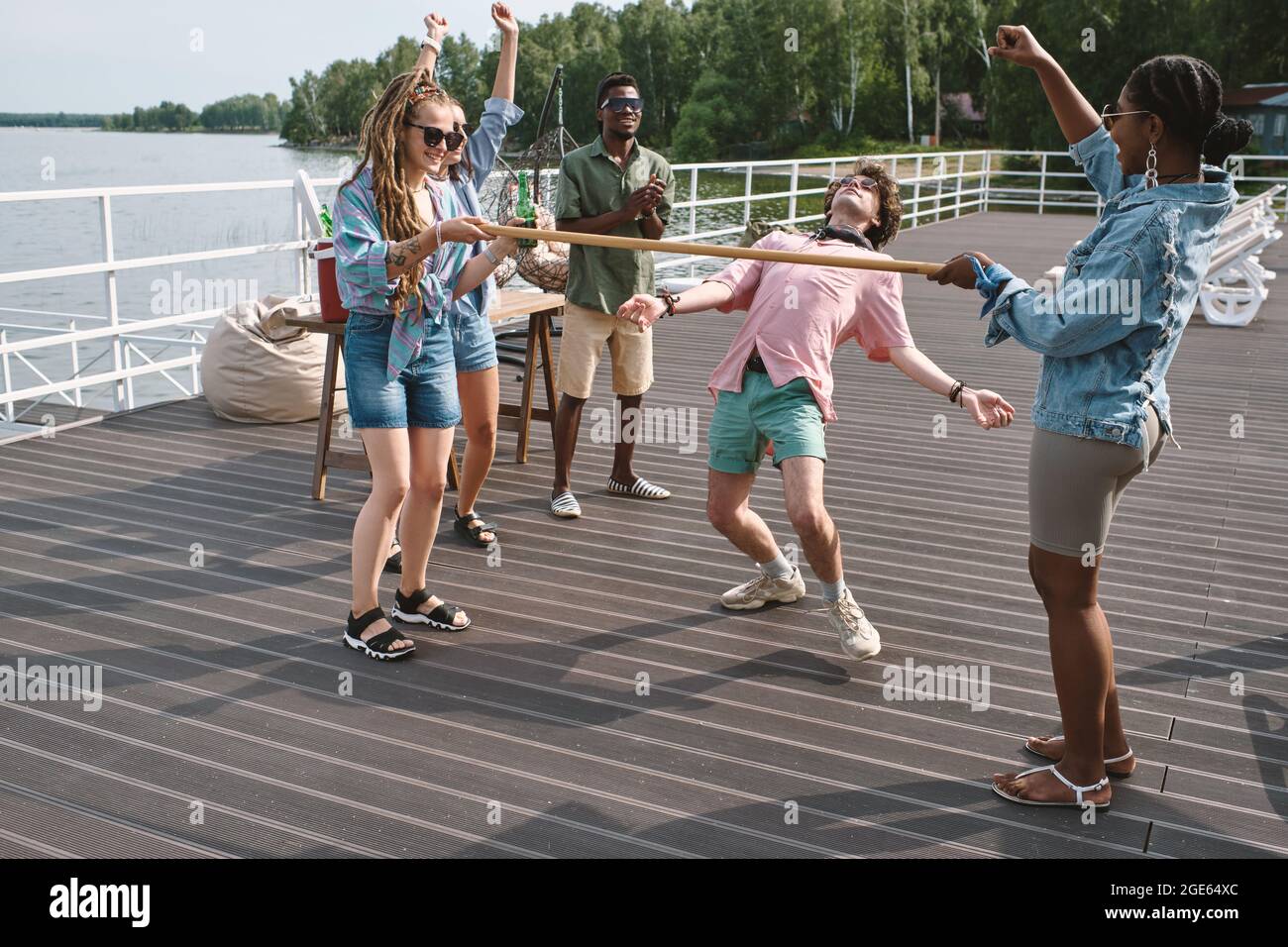 Friends cheering for young man bending backwards to walk under vertical bar  playing limbo Stock Photo - Alamy