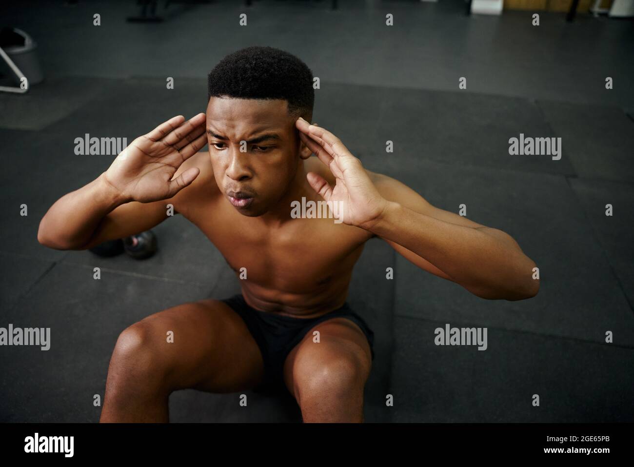Young African American male doing sit-ups on the floor in the gym. Mixed race male personal trainer exercising shirtless indoors. High quality photo Stock Photo