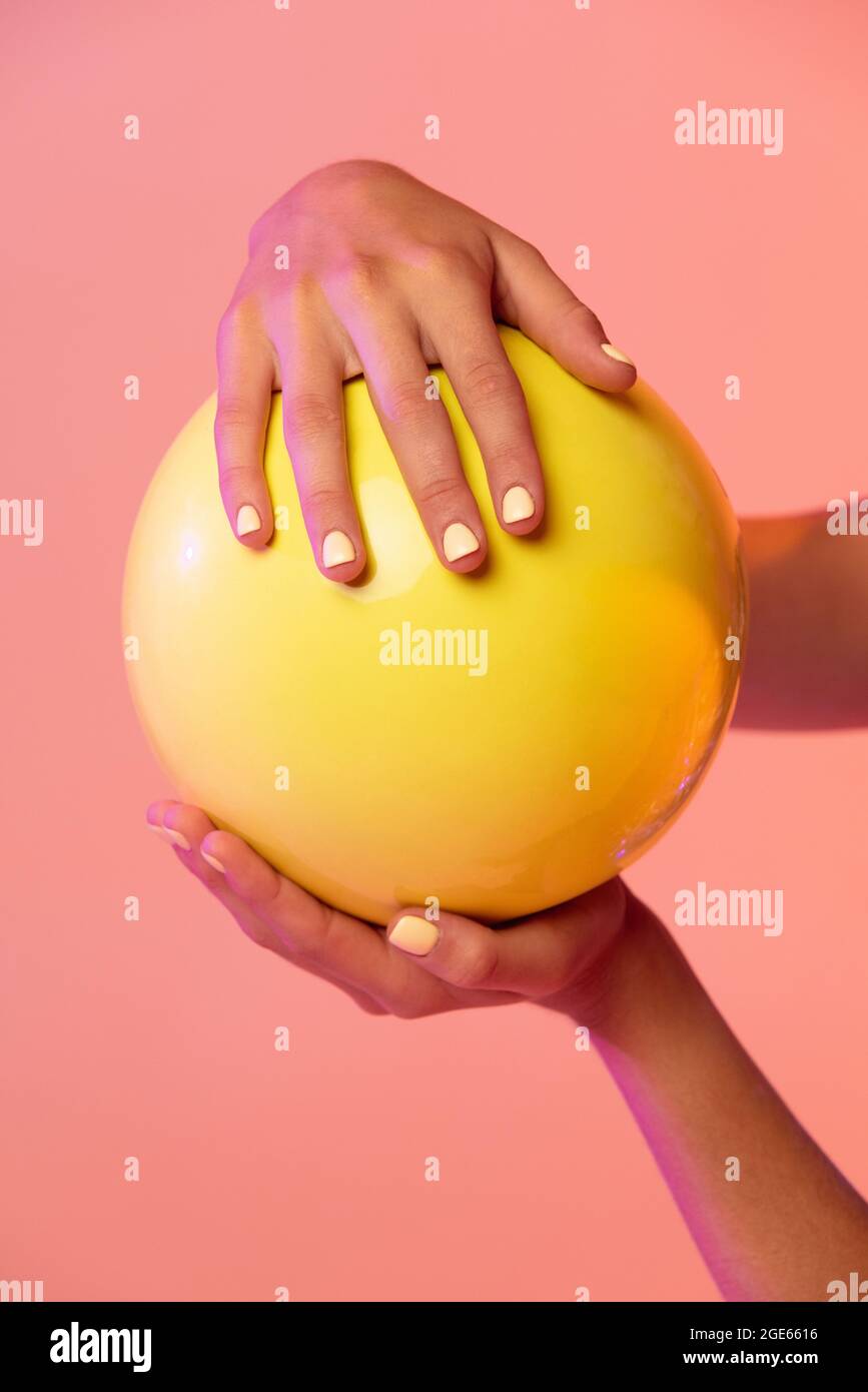Close-up female hands and rhythmic gymnastics yellow ball isolated on gradient pink yellow studio background with neon filters. Stock Photo