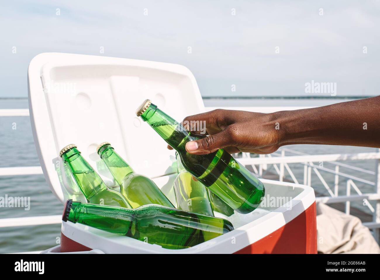 Hand of man taking glass bottle of cold tasty beer out of cooler box when attending party on pier Stock Photo