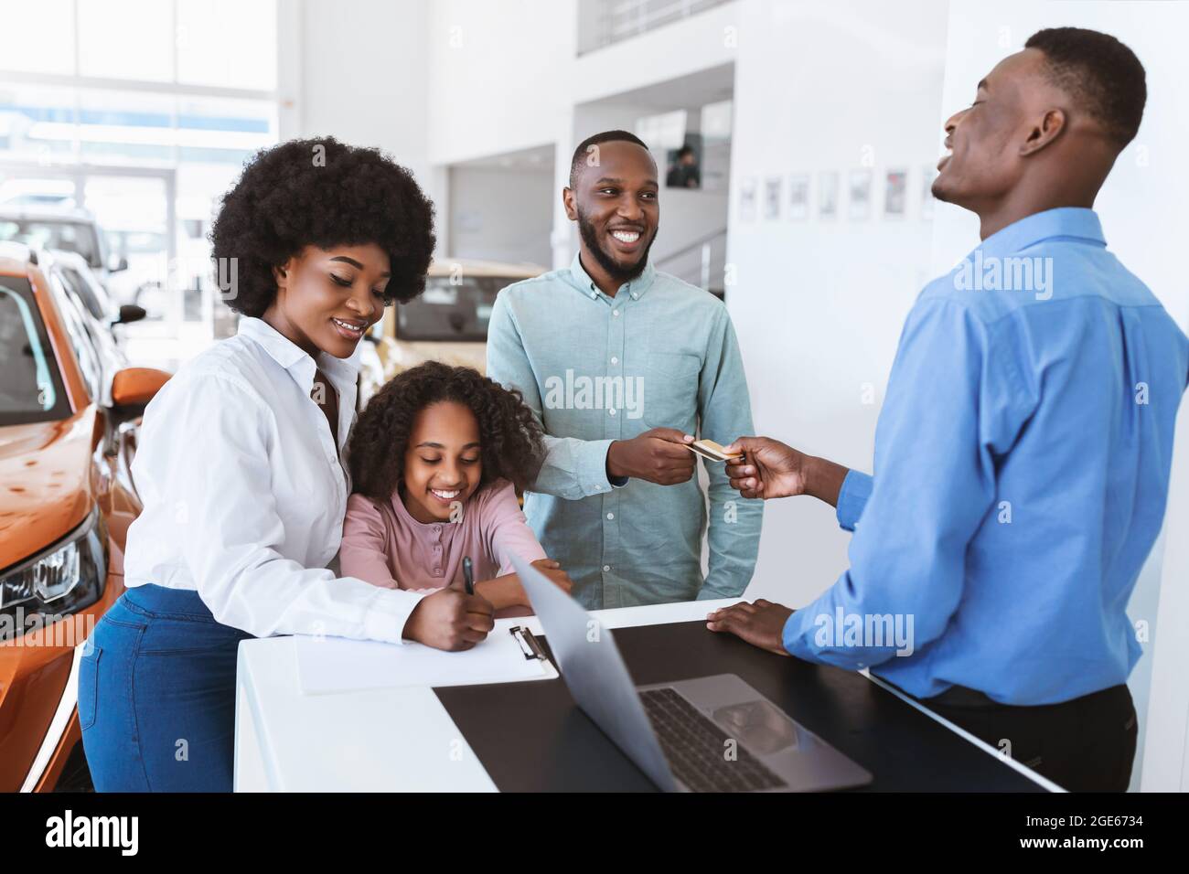 Joyful black family giving credit card to car salesman, paying for new