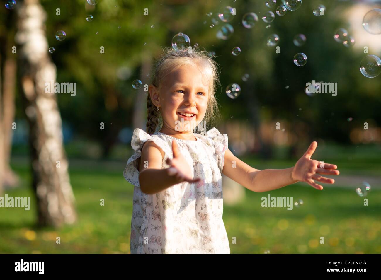 Little cute girl in the summer park blowing bubbles and having fun. Stock Photo