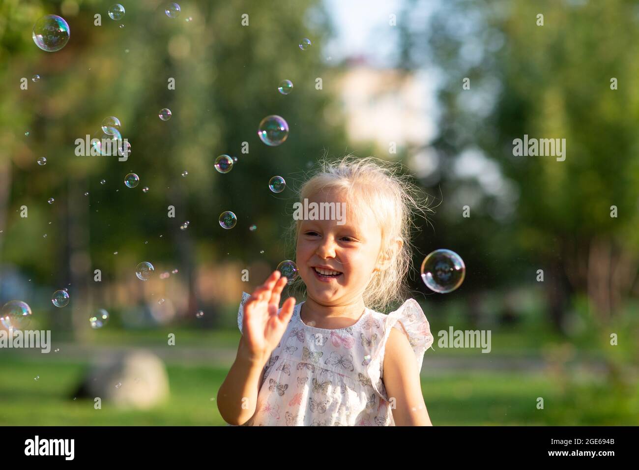 Little cute girl in the summer park blowing bubbles and having fun. Stock Photo