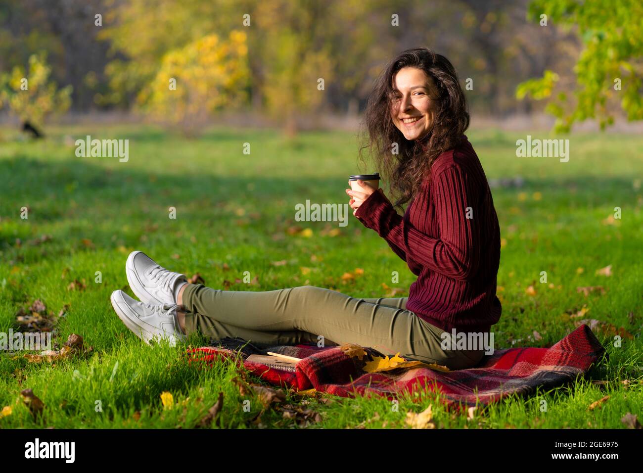 Pretty girl enjoys autumn and the beauty of nature sitting on a green ...