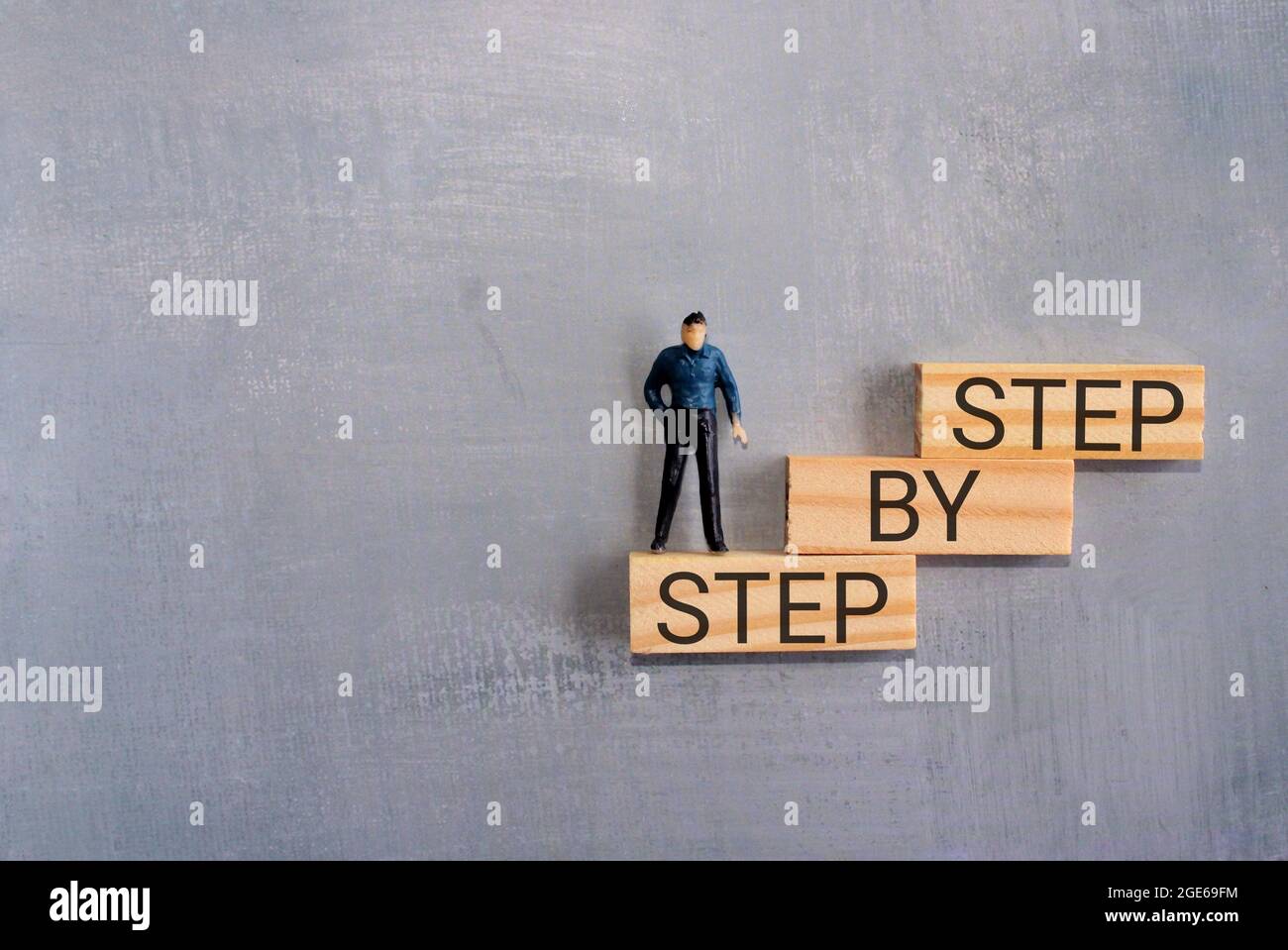 Ladder of success growth concept. Miniature man on wooden block stacking as step stair with text STEP BY STEP. Copy space for text Stock Photo