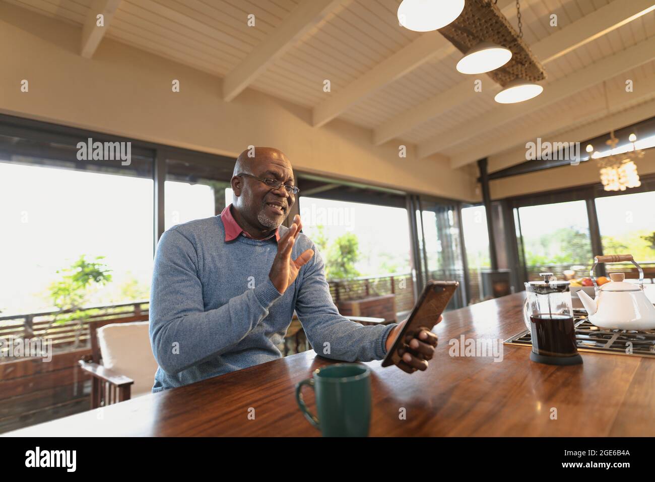 Smiling senior african american man siting in the modern kitchen and making video call Stock Photo