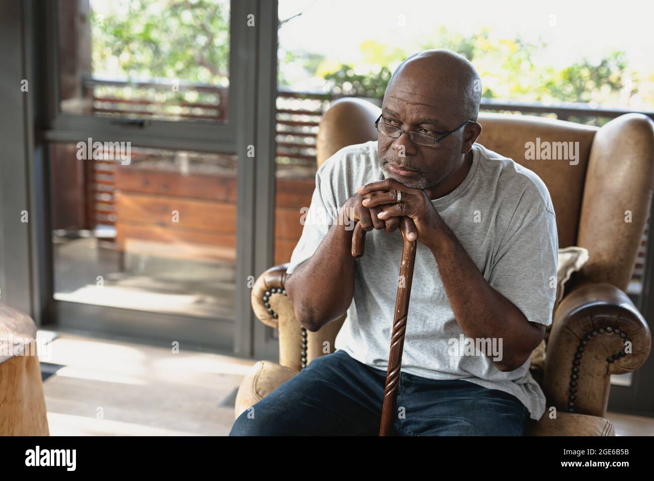 Thoughtful senior african american man sitting on armchair and leaning on the walking stick Stock Photo