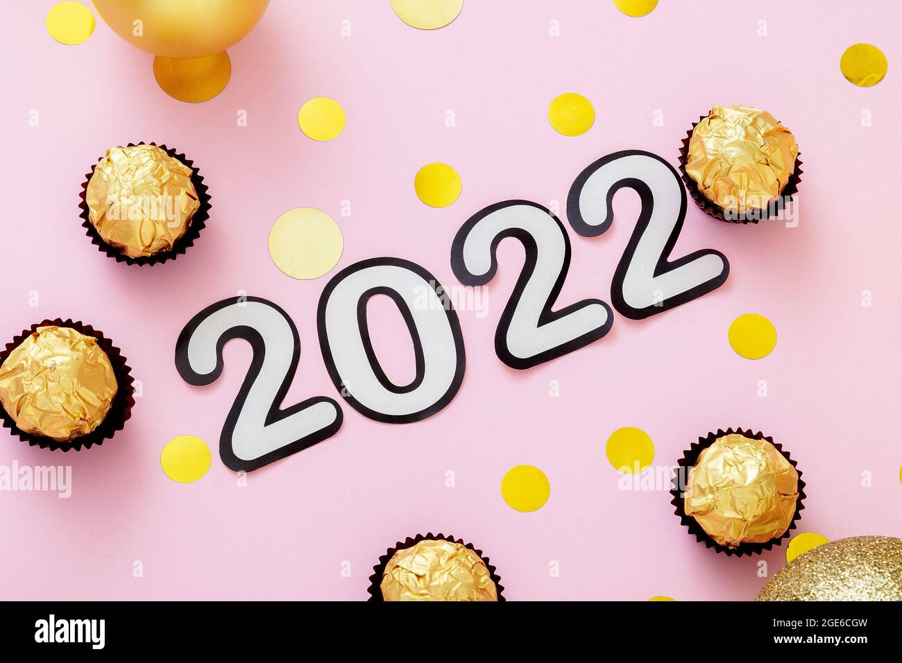2022 text with Christmas decorations candies Sweets gold confetti on pink color background. Goals 2022 lettering in Happy New Year style. Stock Photo