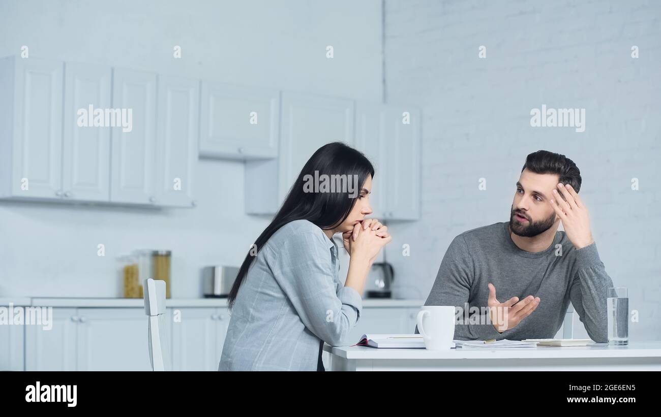 man gesturing while discussing finances with woman in kitchen Stock Photo