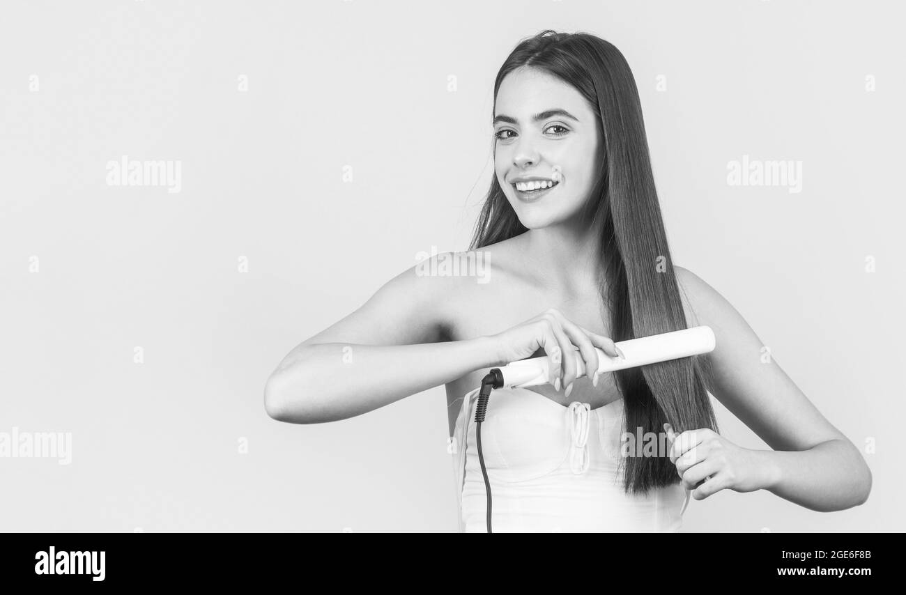 Hairstyle. Beautiful smiling woman ironing long hair with flat iron. Portrait of young beautiful