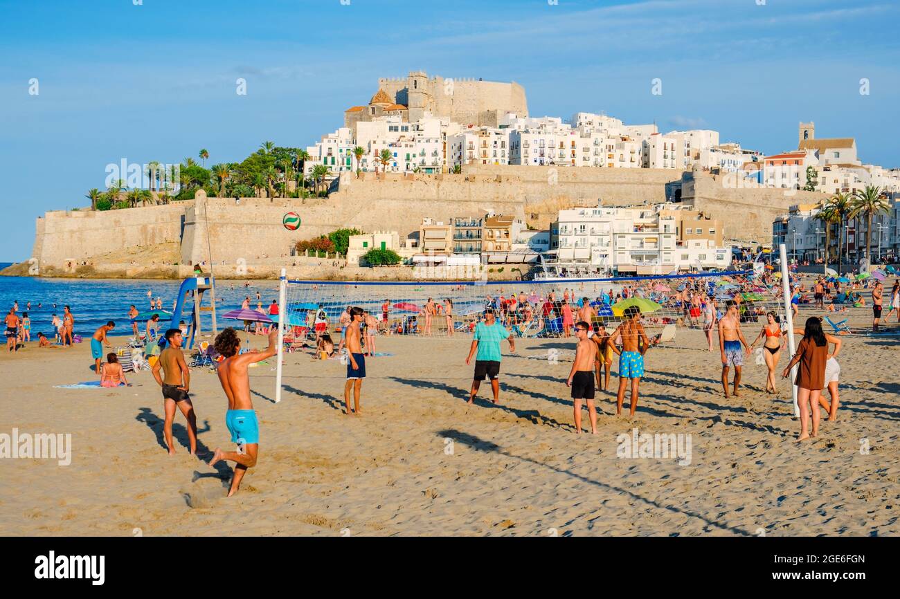 PENISCOLA, SPAIN - AUGUST 2, 2021: People enjoying on the beach in Peniscola, in Valencia, highlighting its fortified walls on the background. It is a Stock Photo