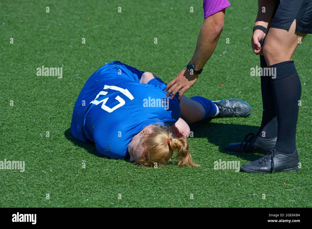 Injured girl football player lying on the soccer field double up with