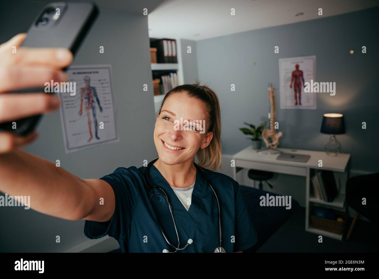 Caucasian female nurse standing in doctors office taking selfie on cellular device  Stock Photo