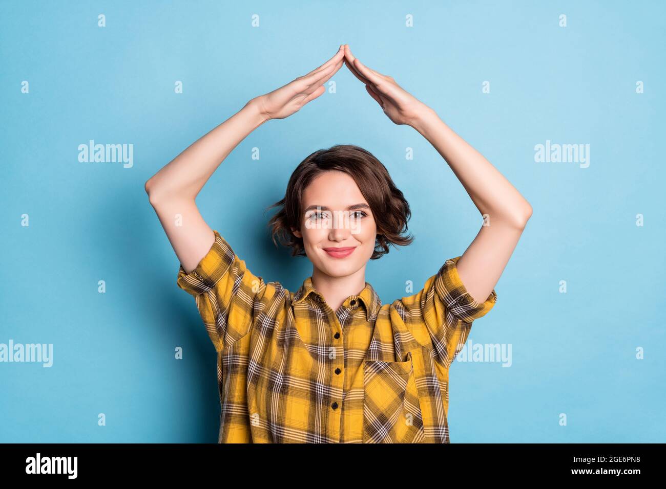 Photo of cheerful secure lady raise hands show roof figure wear checkered shirt isolated blue color background Stock Photo