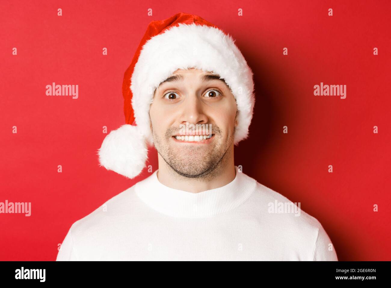 Closeup of handsome guy in santa hat, biting lip and looking with