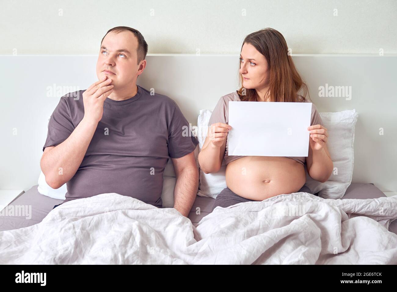 Doubt worried man and a pregnant woman lie in bed with a sheet A4 paper
