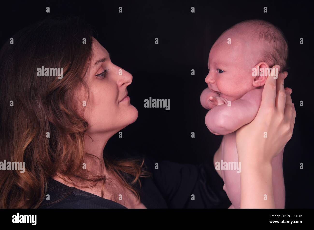 Happy woman mother holds a newborn baby boy in her arms, black studio background. Mom smiles with a child in her hands Stock Photo