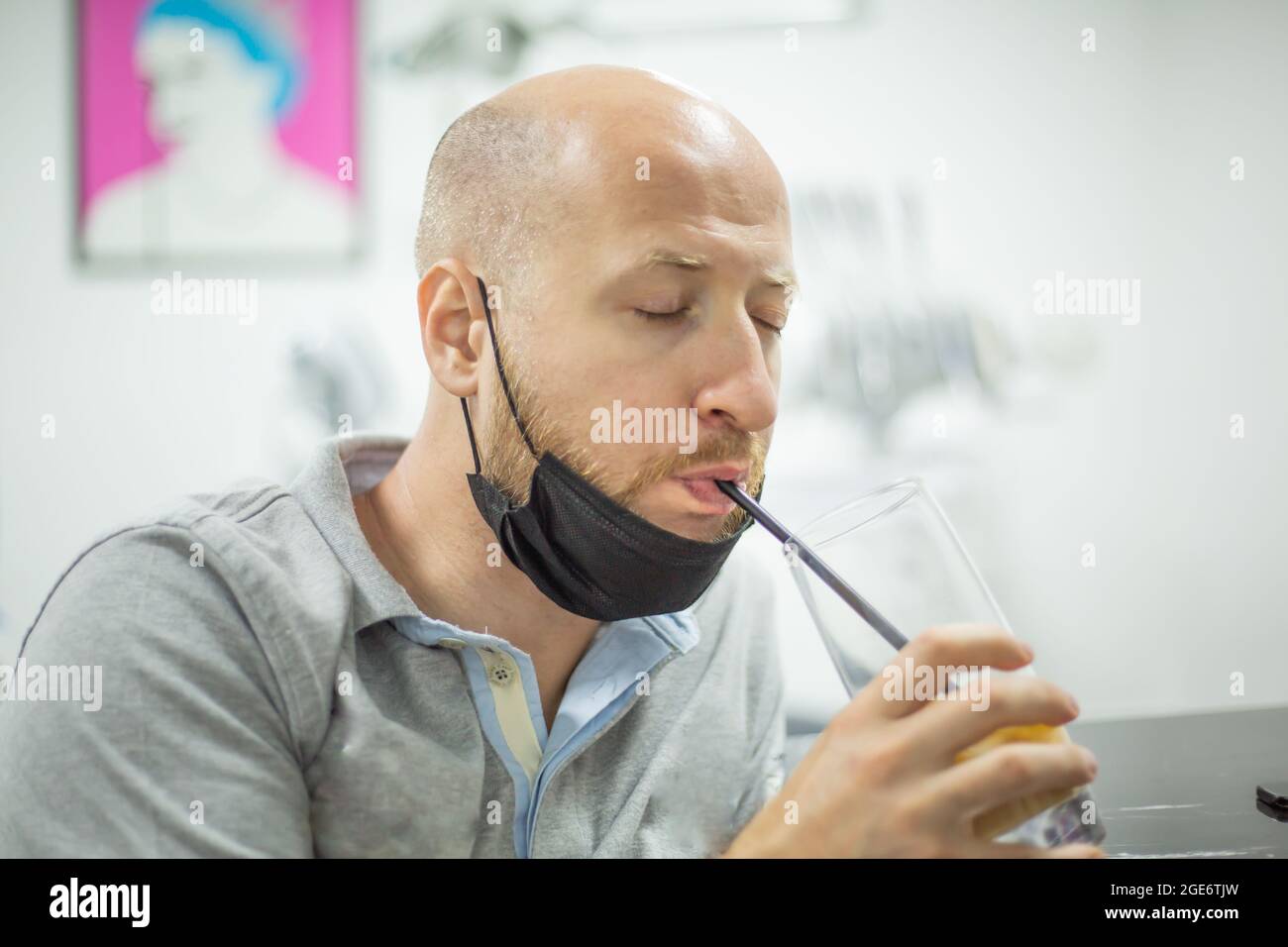 Caucasian male with mask and closed eyes is drinking his long drink with a straw. Stock Photo