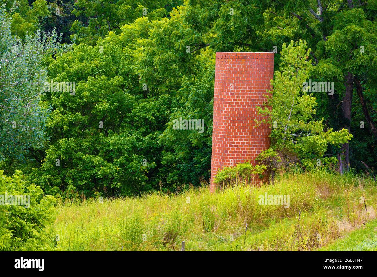 A brick silo sits in the corner of a pasture and a forest of trees in rural Virginia. Stock Photo