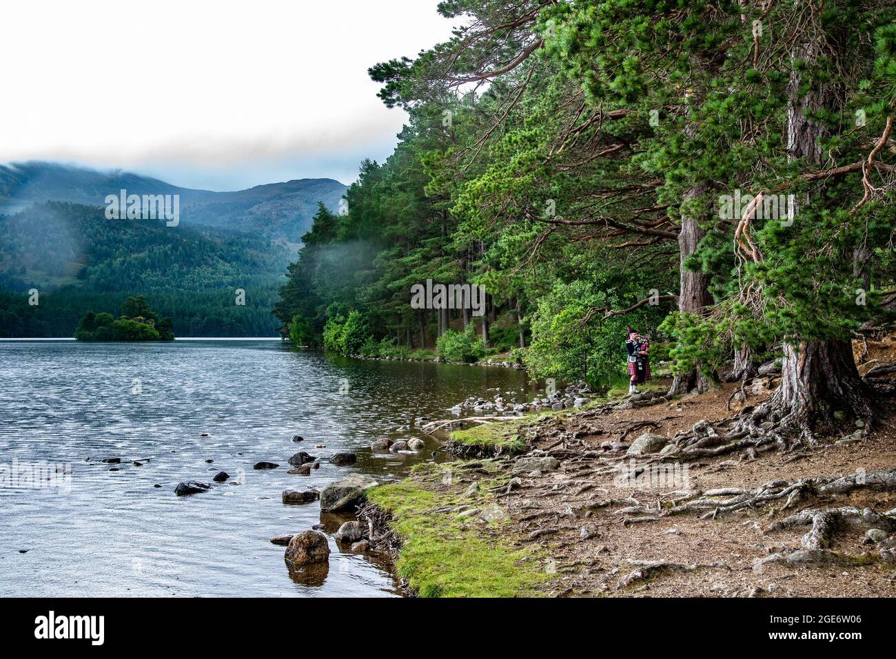 A Scottish piper playing the bagpipes at Loch Eilein, Aviemore, Cairngorms National Park, Scottish Highlands, UK Stock Photo
