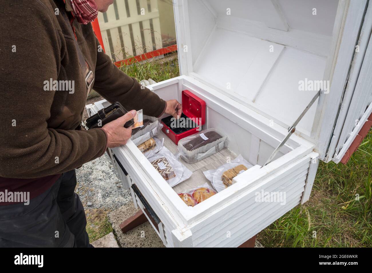 Woman buying food from a roadside stand with an honesty box at Baltasound on the island of Unst, Shetland. Stock Photo