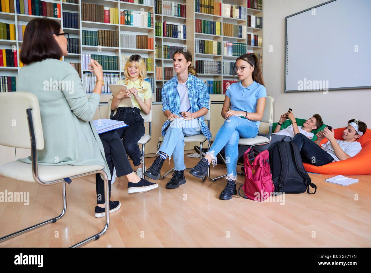 Female mentor teacher working with male teenage high school students in library Stock Photo