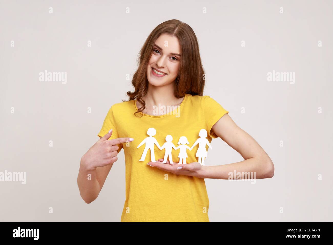 Kind smiling positive teenager girl in yellow t-shirt pointing at paper chain people which holding in hands, happy family, relationships, parenthood. Stock Photo