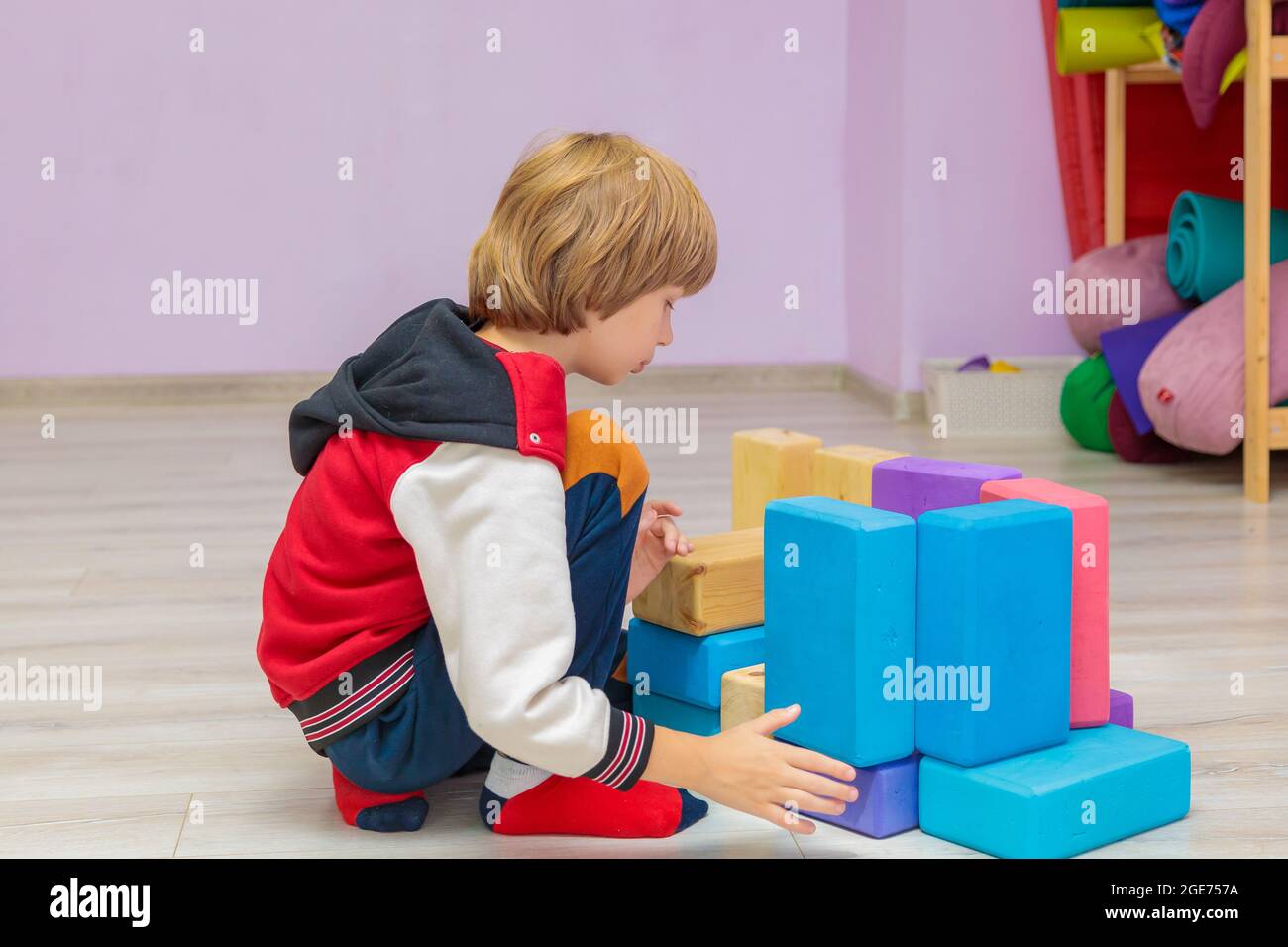 In the hall, the child collects toy cubes. The boy plays in the hall with sports items. Stock Photo