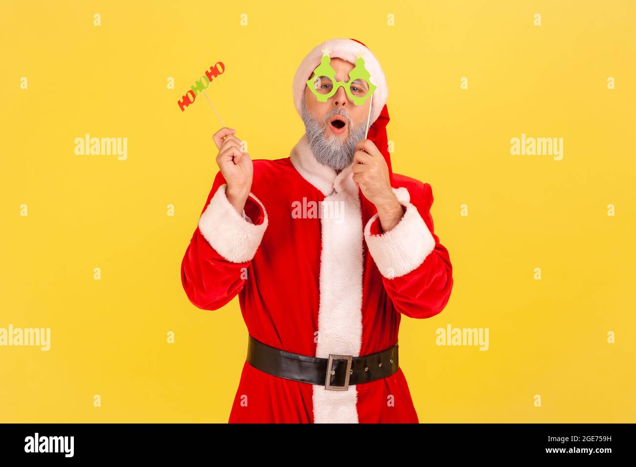 Excited elderly man with gray beard wearing santa claus costume holding paper cards on sticks, celebrating christmas and congratulating with new year. Stock Photo