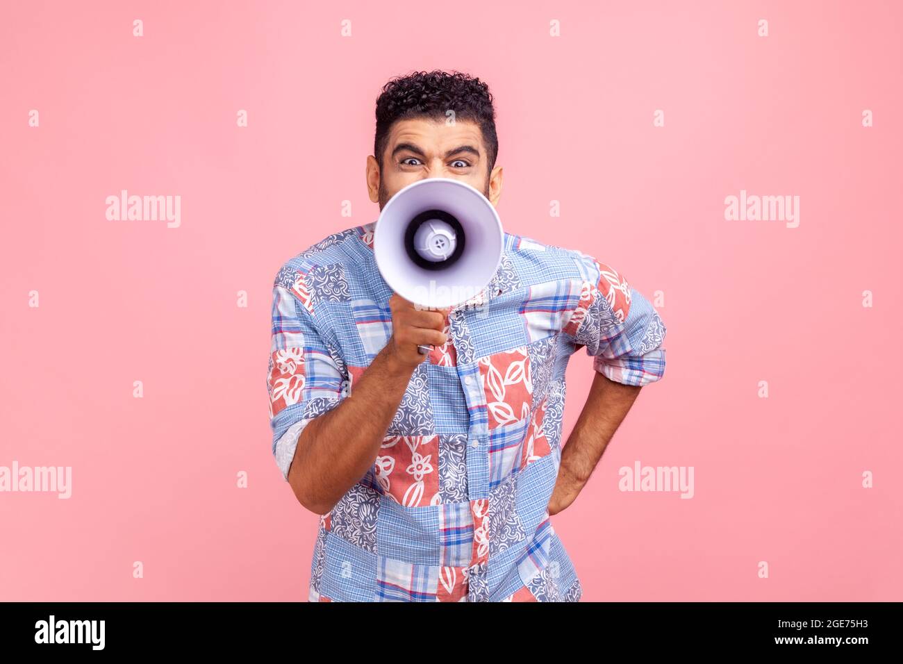 Nervous man with beard in casual style shirt screaming at megaphone, making announce, protesting, looking at camera with angry expression. Indoor stud Stock Photo