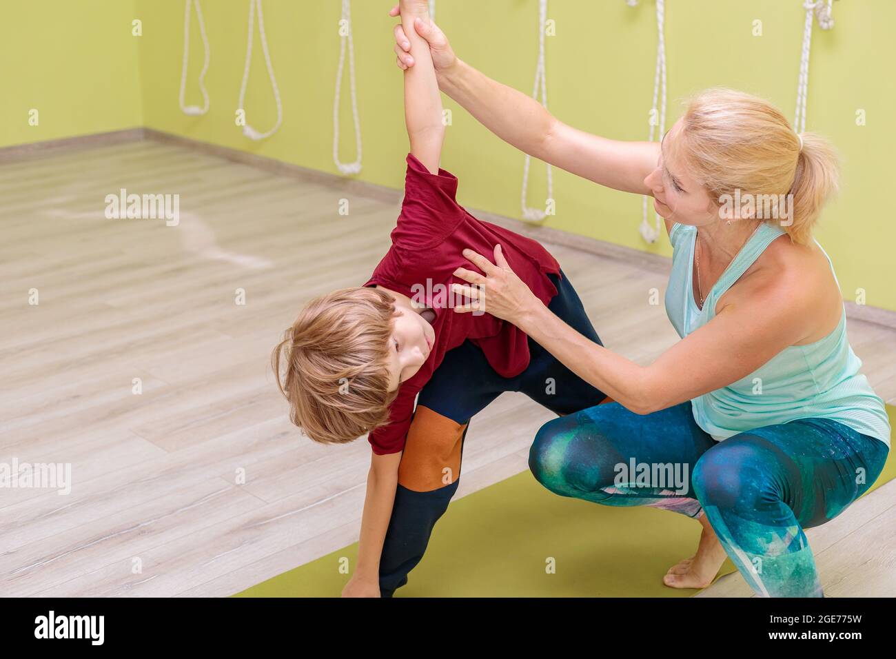 A woman instructor in a sports uniform is engaged in yoga with a boy. The girl corrects the asanas for the child. Calm, balance and concentration conc Stock Photo
