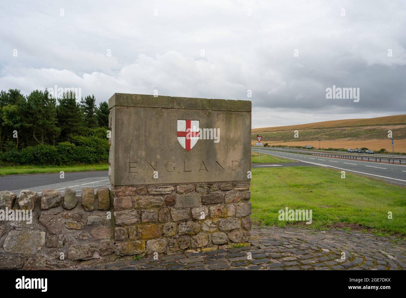 Stone England sign with St Georges cross at border with Scotland on A1 road. Background of road and greenery. No people. Stock Photo