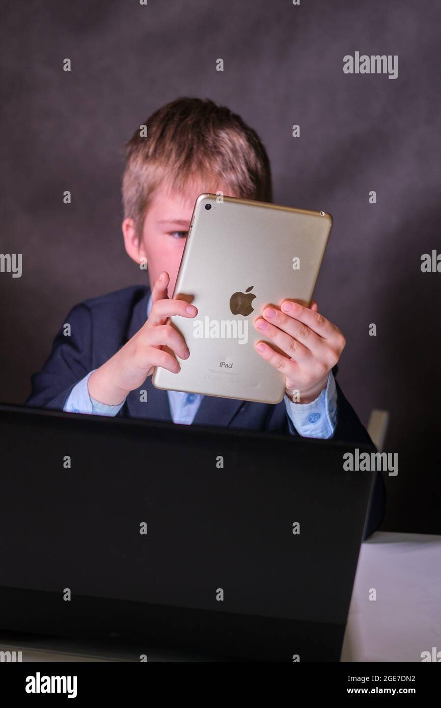 A happy boy in a school suit with a digital tablet in his hands, copy space on a dark studio background - Moscow, Russia, February 05, 2021 Stock Photo
