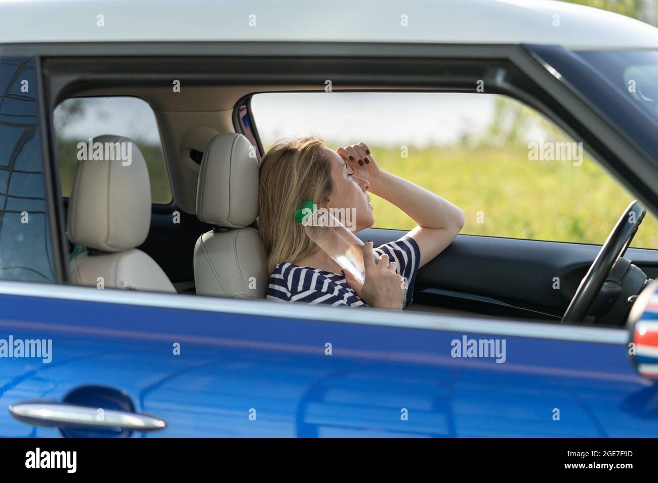 Exhausted girl driver suffering from headache, heat, hot weather applies bottle of water to neck Stock Photo