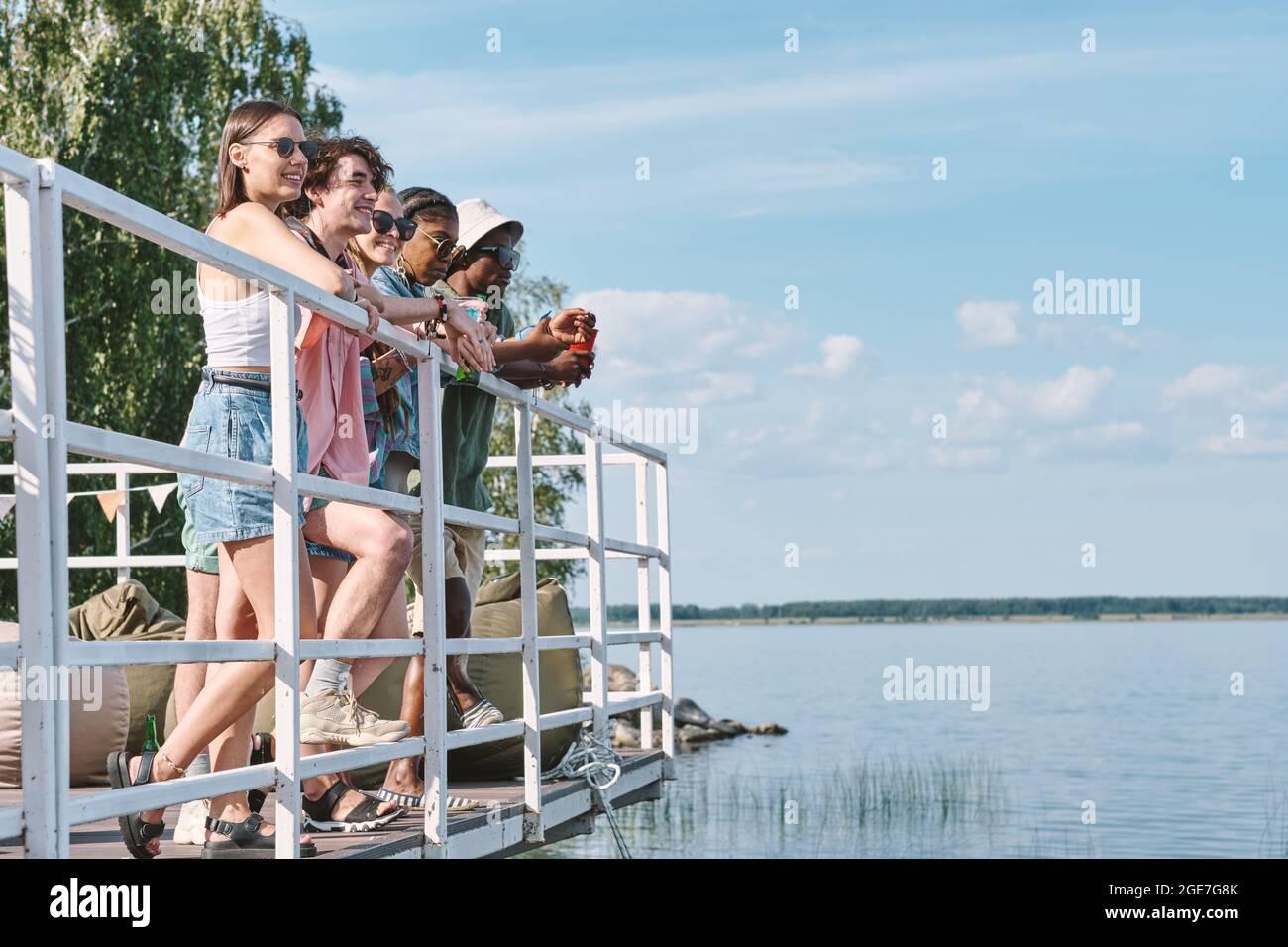 Diverse group of happy friends standing on pier and looking at water Stock Photo