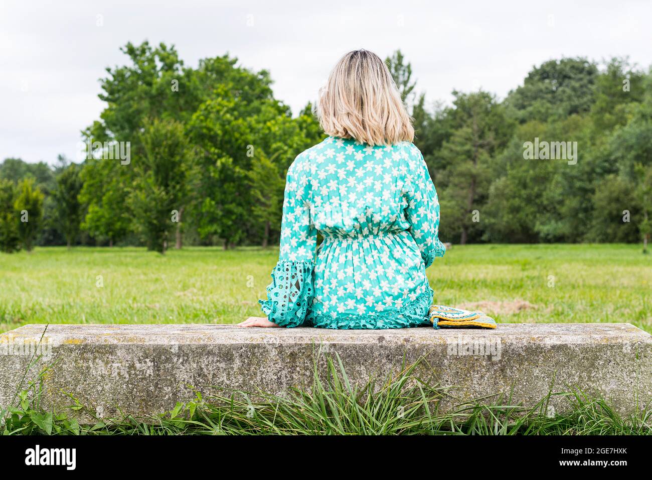 Model sitting with her back to the camera on a bench in a green area of Asturias, Spain.The woman is wearing a nice long green dress.The photo is ta Stock Photo