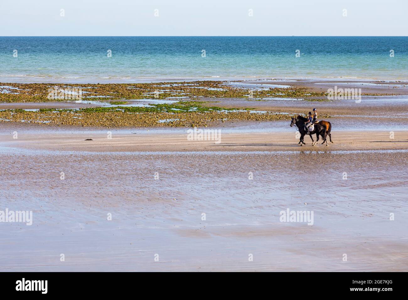 Two horse riders enjoy walking along a deserted beach at low tide at Climping, West Sussex, England. Stock Photo