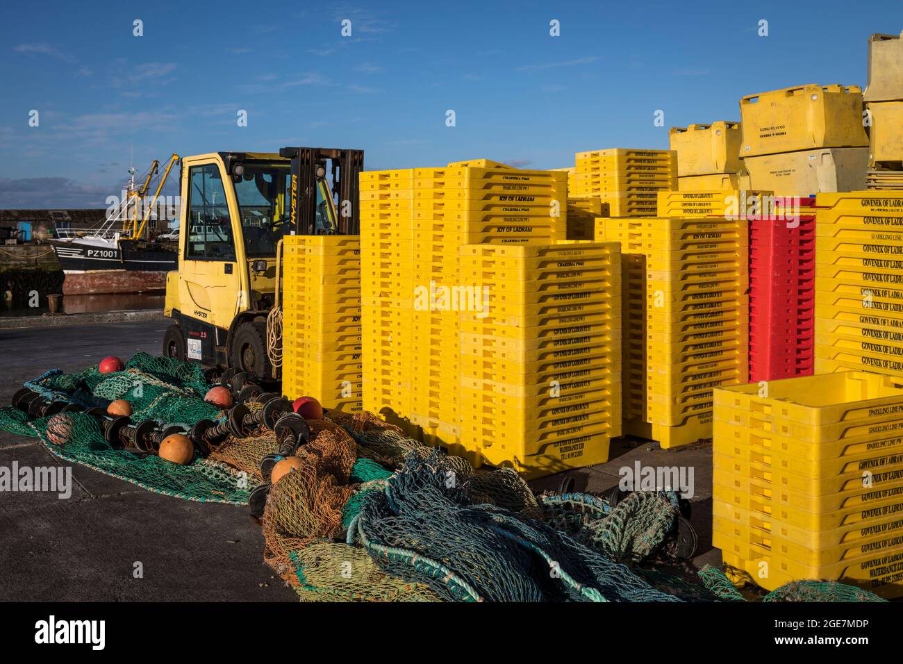 Stacks of bright yellow plastic fish crates and nets on the dockside in Newlyn harbour, Cornwall, England. Stock Photo