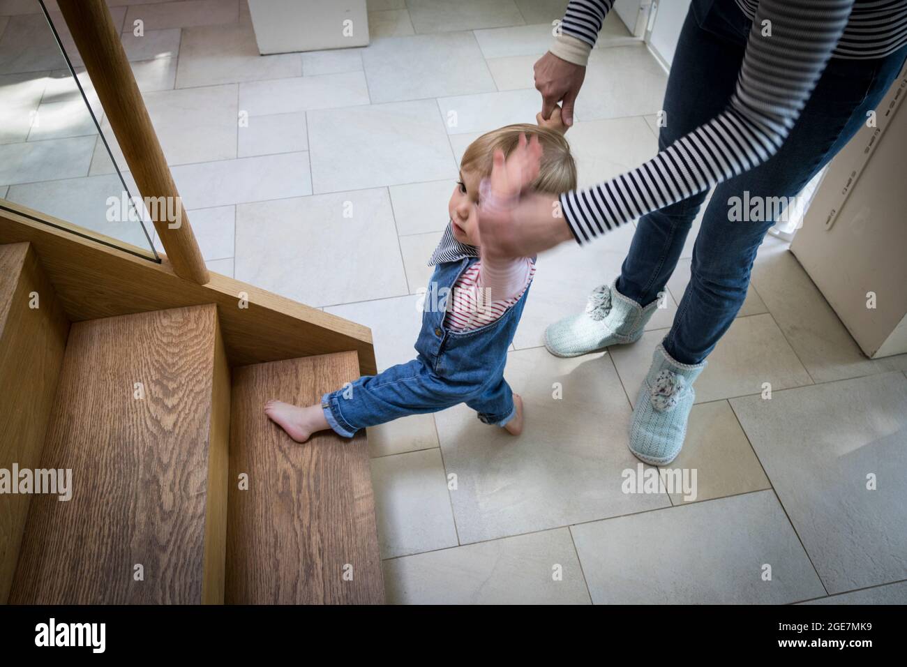 Toddler about to walk up wooden staircase assisted by mother, England. Stock Photo