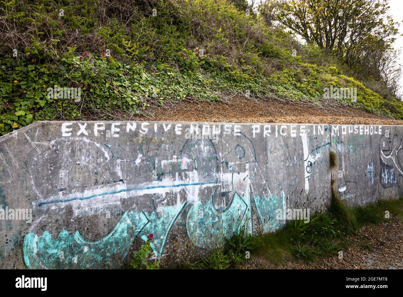 Graffiti on a wall alongside a footpath, complaining about local house prices, Mousehole, Cornwall, England. Stock Photo