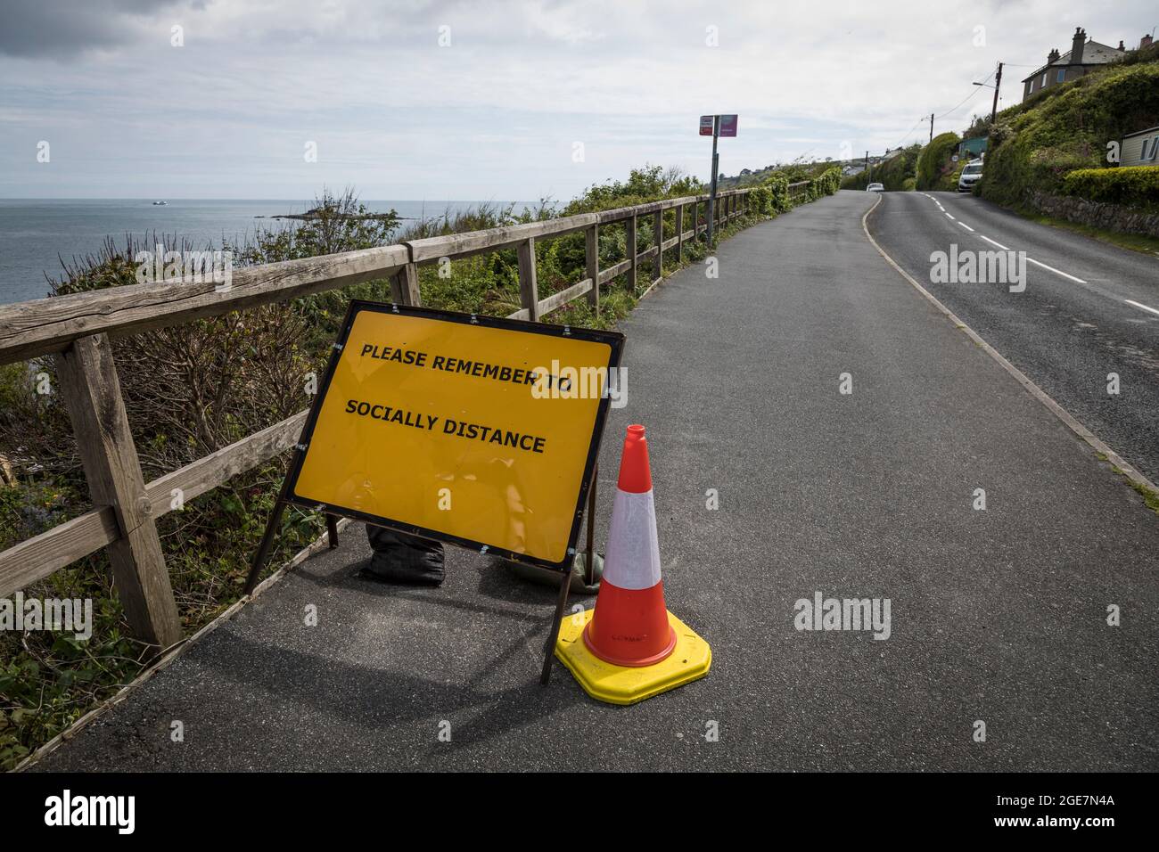 Roadside warning sign and cone reminding pedestrians to 'socially distance' during Covid-19 outbreak, Cornwall, England. Stock Photo